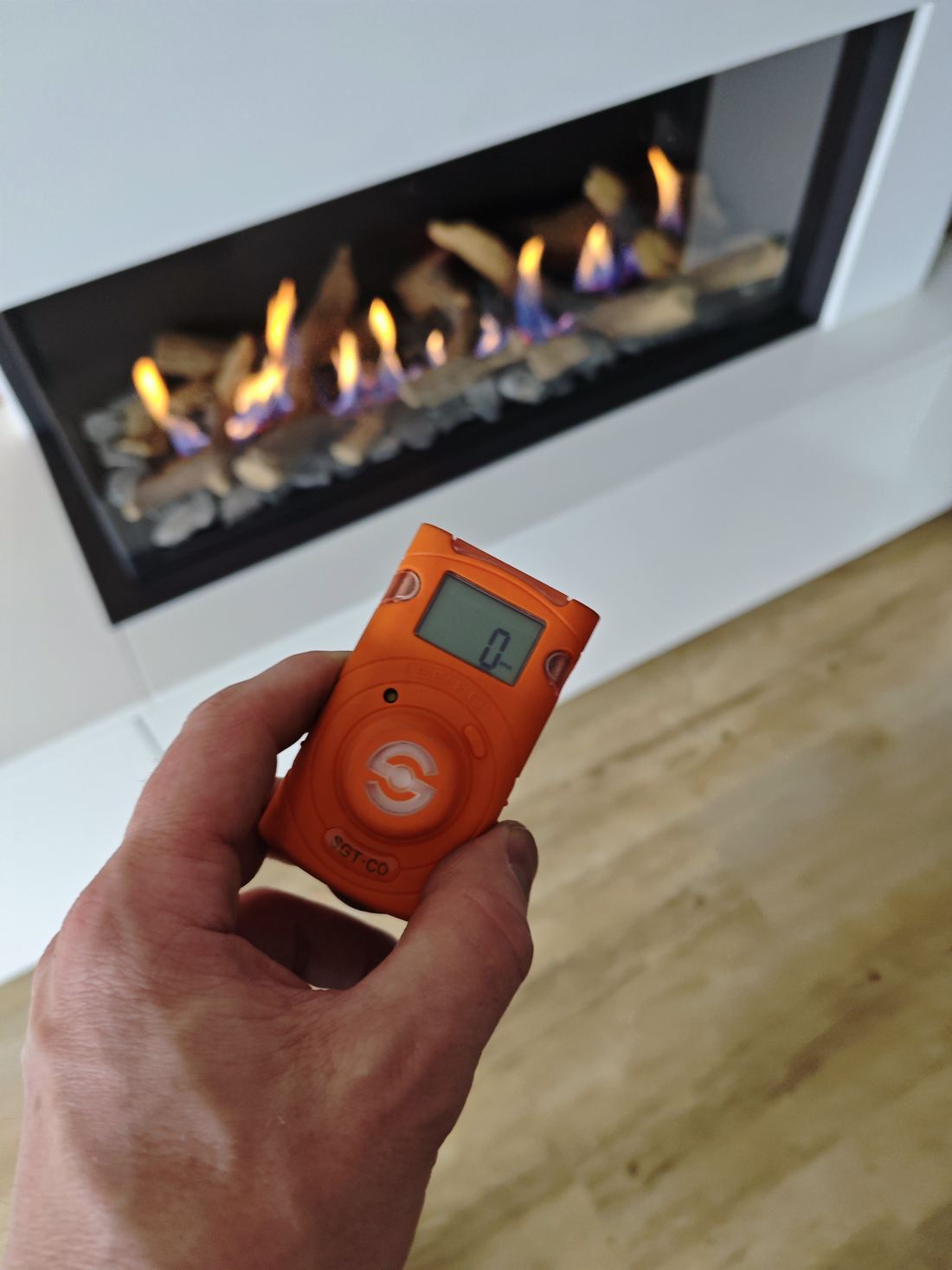 Hand met CO-meter die nul ppm aanwijst voor een brandende gashaard
